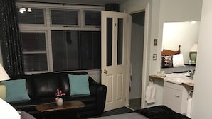 A bedroom with a large bed, a black leather sofa, a small table with a vase, and a window with blinds. - Admirals Lodge Picton (Picton)