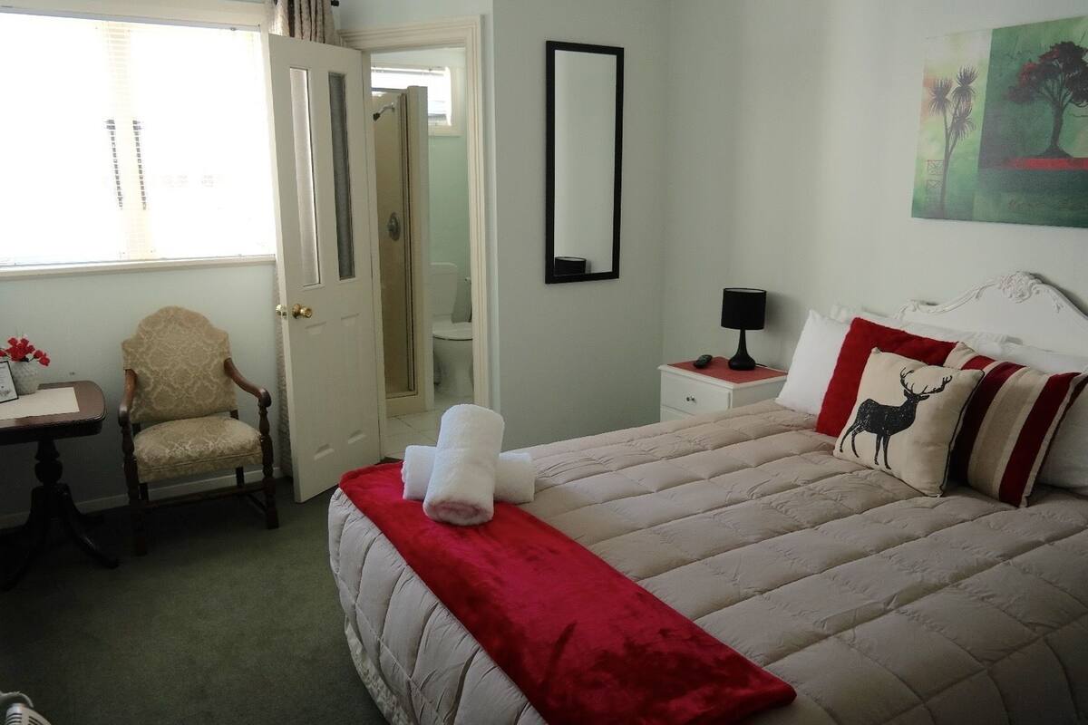 A hotel room with a bed, a chair, a nightstand, a mirror, and a painting on the wall.