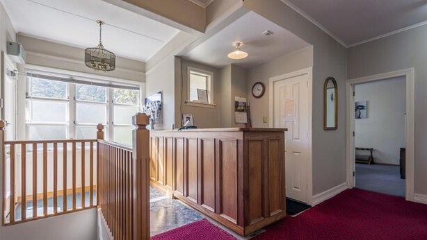A hallway with a wooden railing, a red patterned carpet, a wooden bench, and a door with a clock. - Admirals Lodge Picton (Picton)
