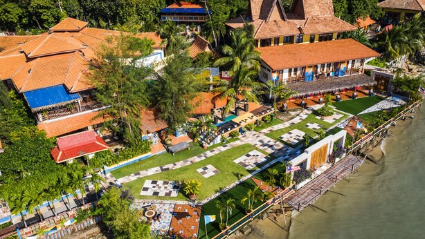 Vista aérea de un complejo turístico con varias edificaciones, un patio central y ubicación frente a la playa.