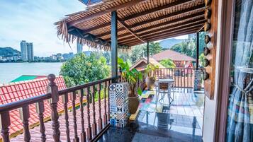 A balcony with a tiled floor, a wooden railing, and a view of a body of water and buildings in the background.