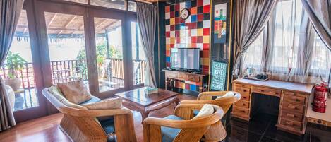 A room with wicker furniture, a wooden desk, a television, and a view of the outdoors.