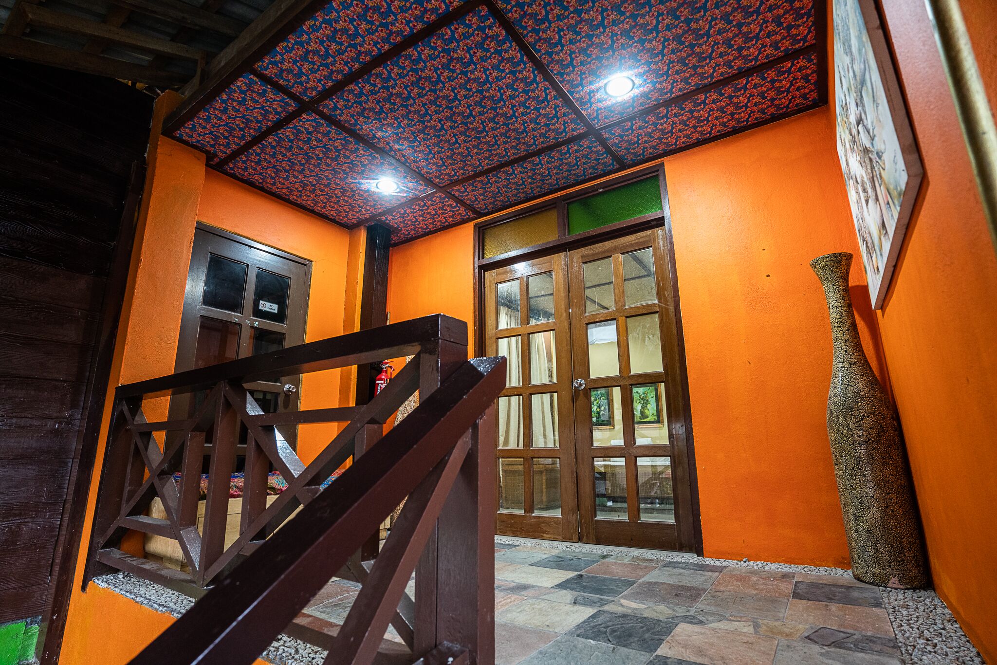 Una habitación con paredes anaranjadas, una escalera de madera, suelo de baldosas y techo estampado.
