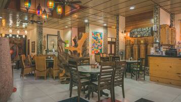 A restaurant with wooden tables and chairs, decorative lanterns, and a colorful wall art piece.