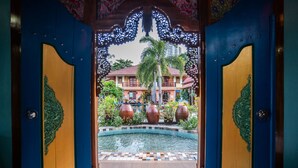 Vista a través de un puerta decorativa, con una piscina y palmeras al fondo.
