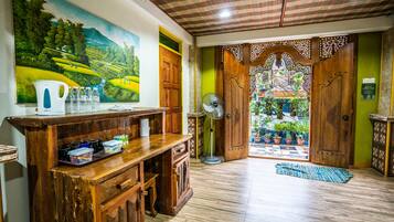 A room with a wooden reception desk, a fan, and a view of a garden through a wooden door.