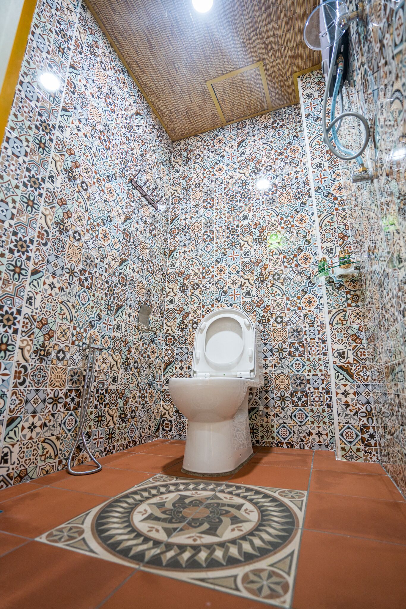 A bathroom with a white toilet, patterned tiles, and a tiled floor with a central design.