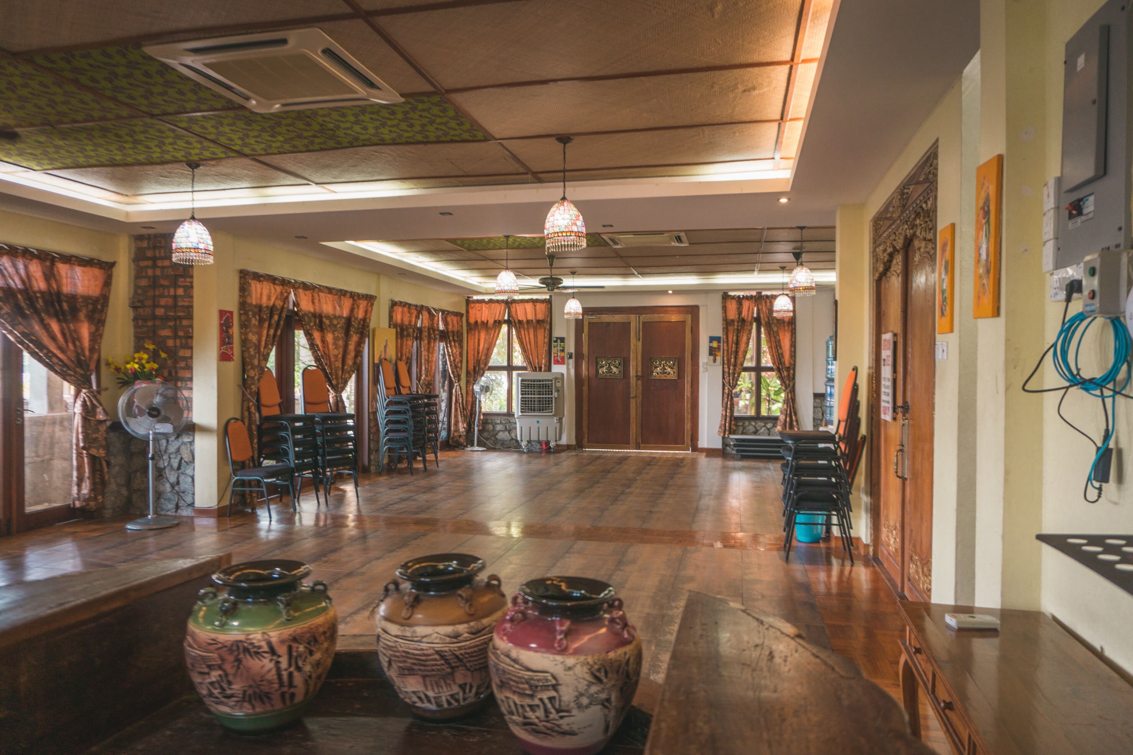 A spacious room with a wooden floor, multiple chairs, a fan, and decorative vases.