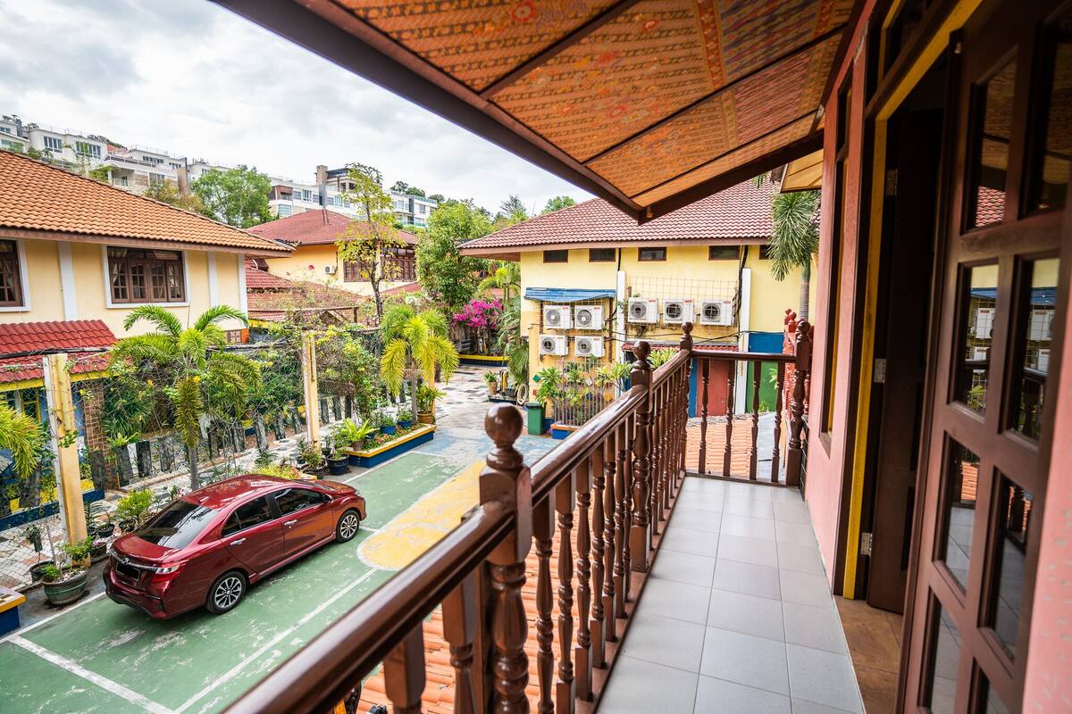 Ein Balkon mit Blick auf eine Straße, ein geparktes Auto und Gebäude mit roten Ziegeldächern.