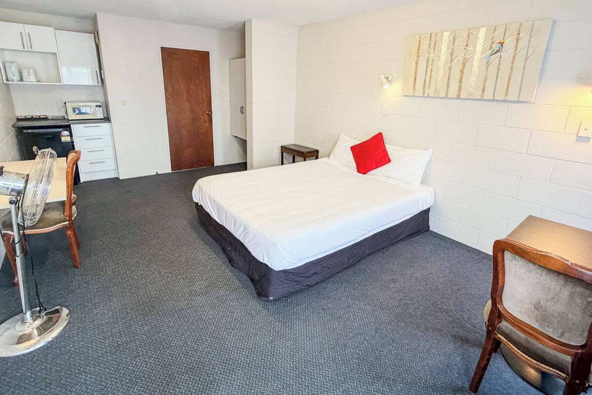 A hotel room with a bed, a desk, a chair, a microwave, and a small table.