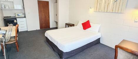 A hotel room with a bed, a desk, a chair, a microwave, and a small table.