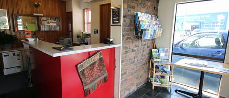 A reception area with a red counter, a brick wall, a window with a view of the street, and a small bookshelf.