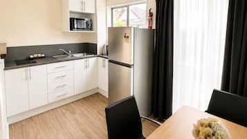 Een moderne keuken met witte kasten, een zwart aanrecht, een roestvrijstalen koelkast en een eethoek met een tafel en stoelen.