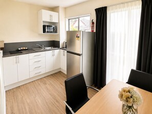 A modern kitchen with white cabinets, a black countertop, a stainless steel refrigerator, and a dining area with a table and chairs. - Midway Pacifica Lodge (Lower Hutt)