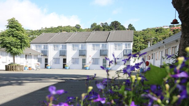 A row of white buildings with grey roofs, arranged in a street with a clear sky. - Midway Pacifica Lodge (Lower Hutt)