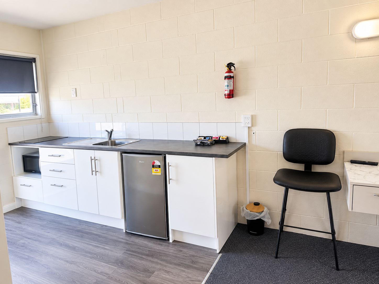 A compact kitchen with a refrigerator, a sink, and a fire extinguisher mounted on the wall.