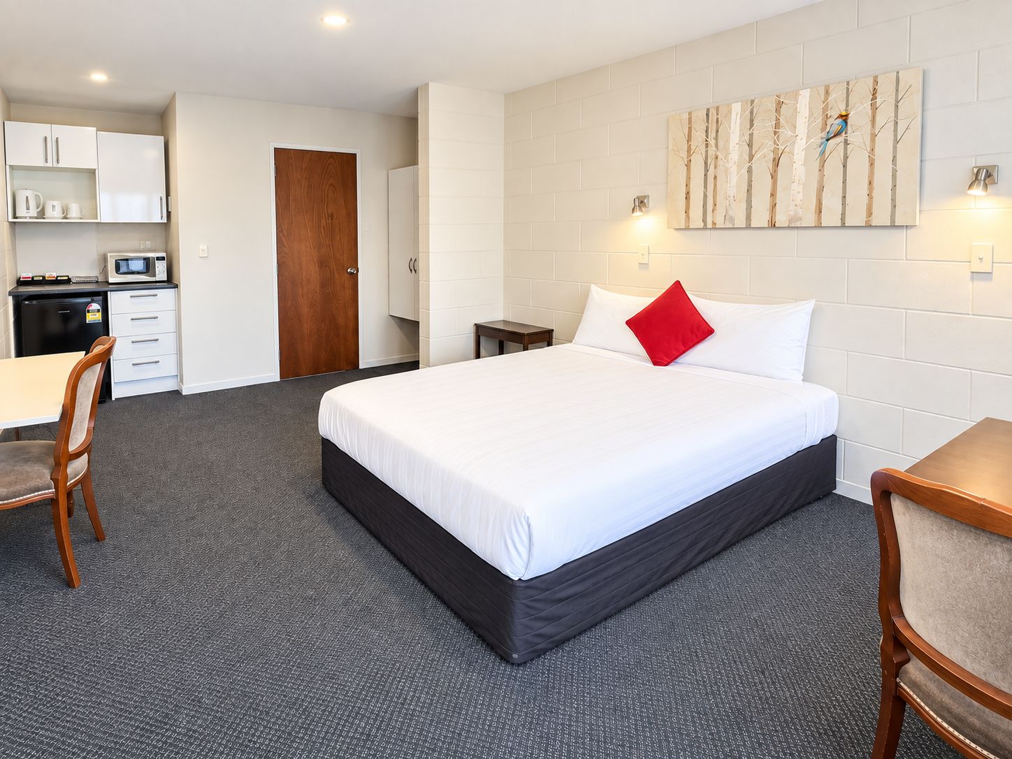 A hotel room with a bed, a desk, a chair, a microwave, a cabinet, and a door.