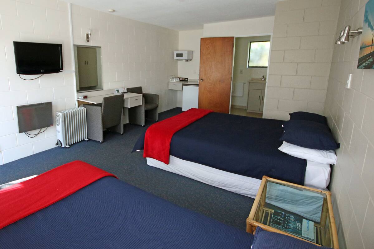 A hotel room with two beds, a desk, a chair, a TV, a microwave, and a small table with a book.