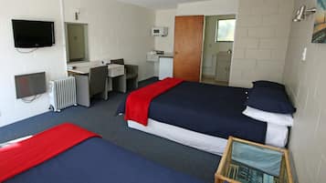 Une chambre d’hôtel avec deux lits, un bureau, une chaise, une télévision, un four à micro-ondes et une petite table avec un livre.