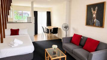 Habitación de hotel con cama, sofá, una mesita con flores, un ventilador y un cuadro en la pared.