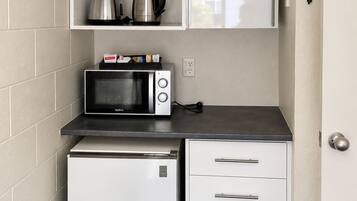 Uma cozinha compacta com micro-ondas, um refrigerador pequeno e uma cafeteira em uma prateleira.