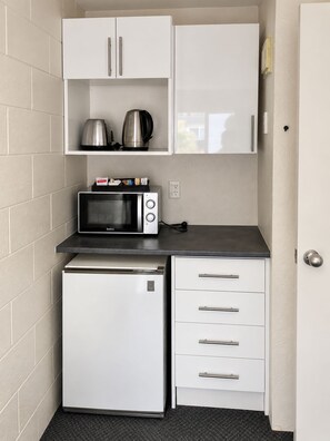 A compact kitchenette with a microwave, a small refrigerator, and a coffee maker on a shelf. - Midway Pacifica Lodge (Lower Hutt)
