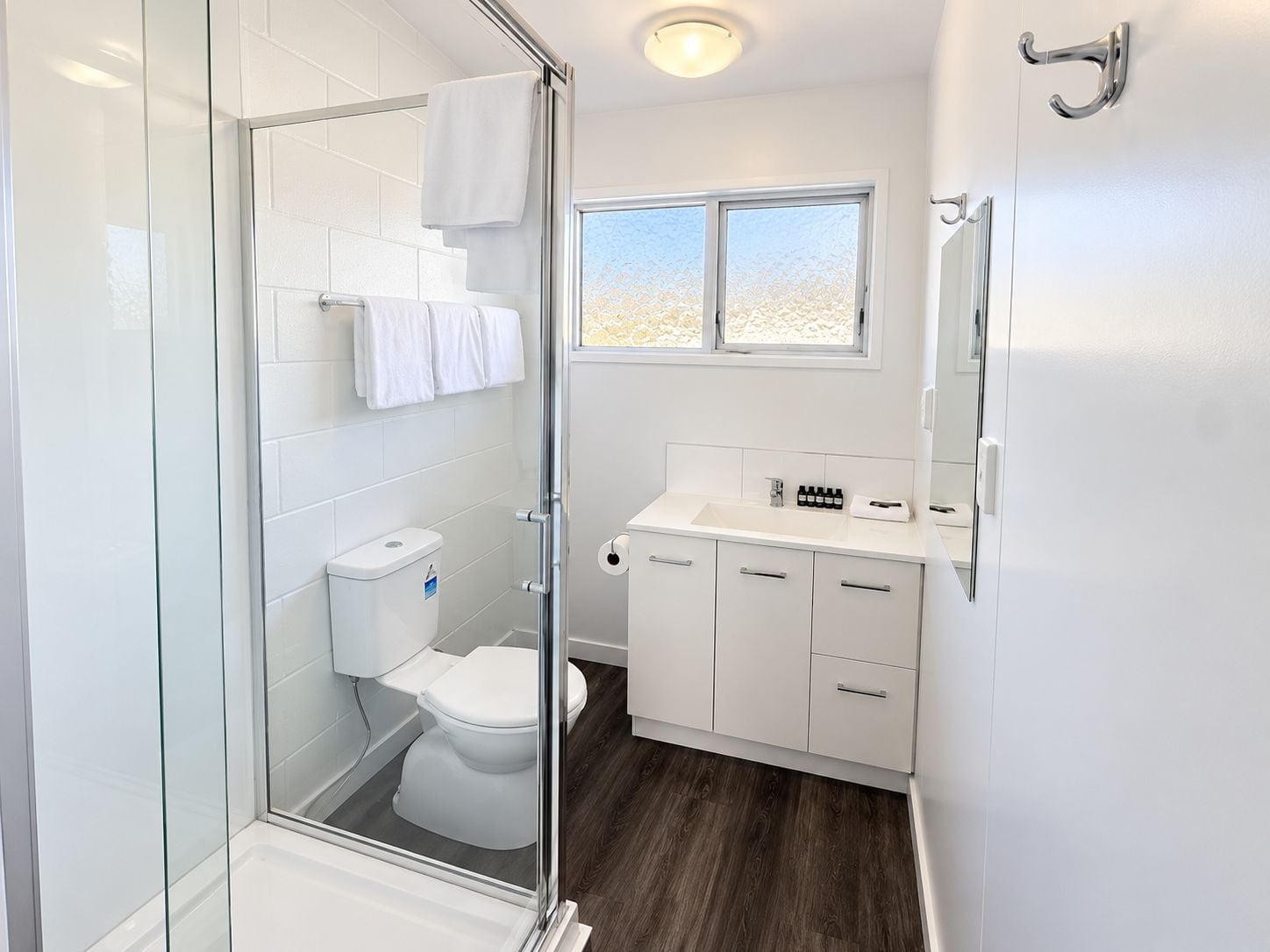 Un baño moderno con cabina de ducha de vidrio, inodoro blanco y lavamanos con armarios.
