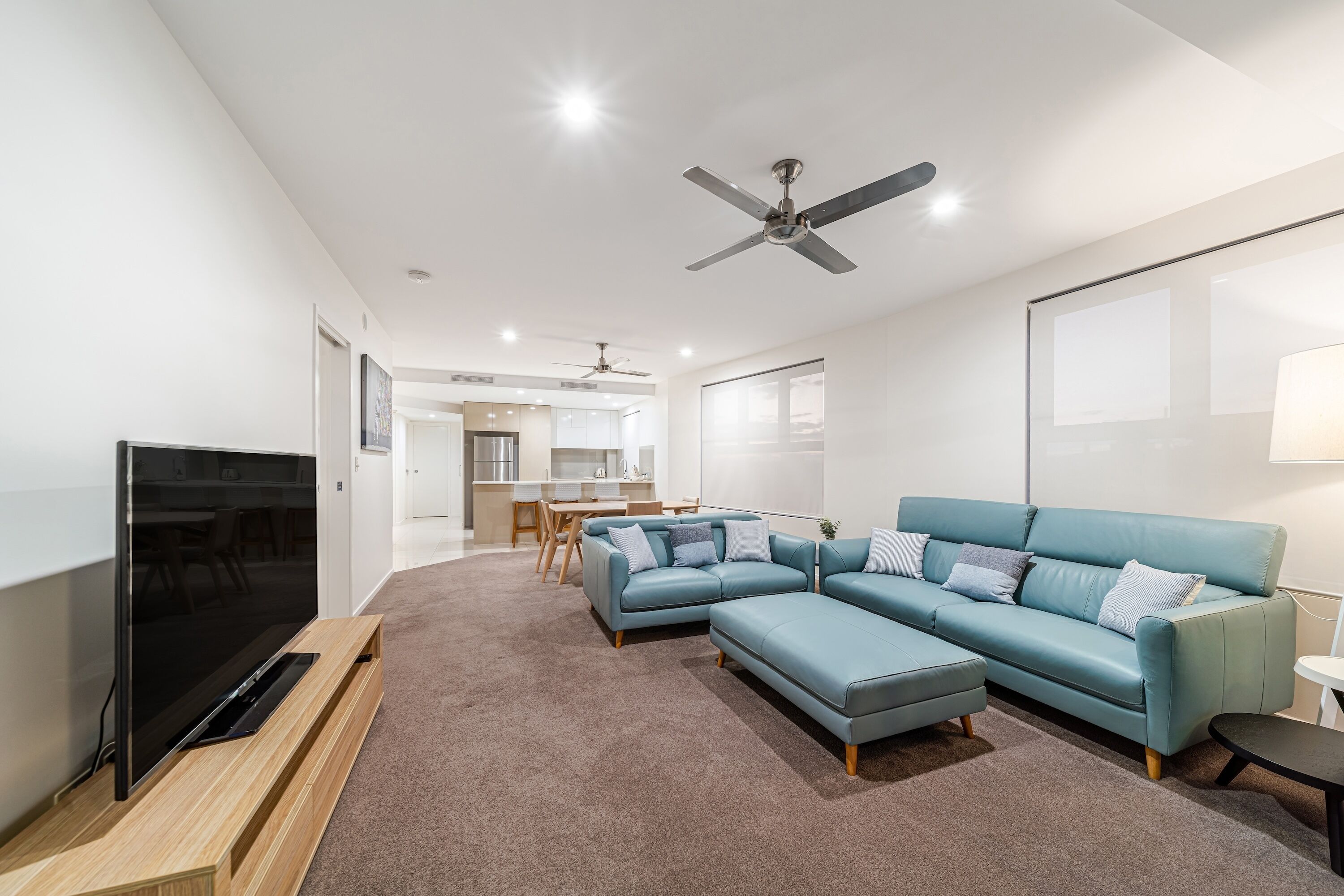 A modern living room with a large flat-screen TV, a blue sectional sofa, and a ceiling fan.