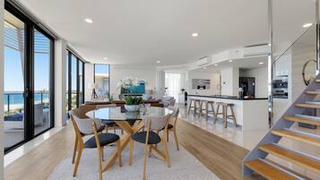 Una cocina moderna con una isla central, un comedor con mesa de vidrio y una escalera que sube a un nivel superior.
