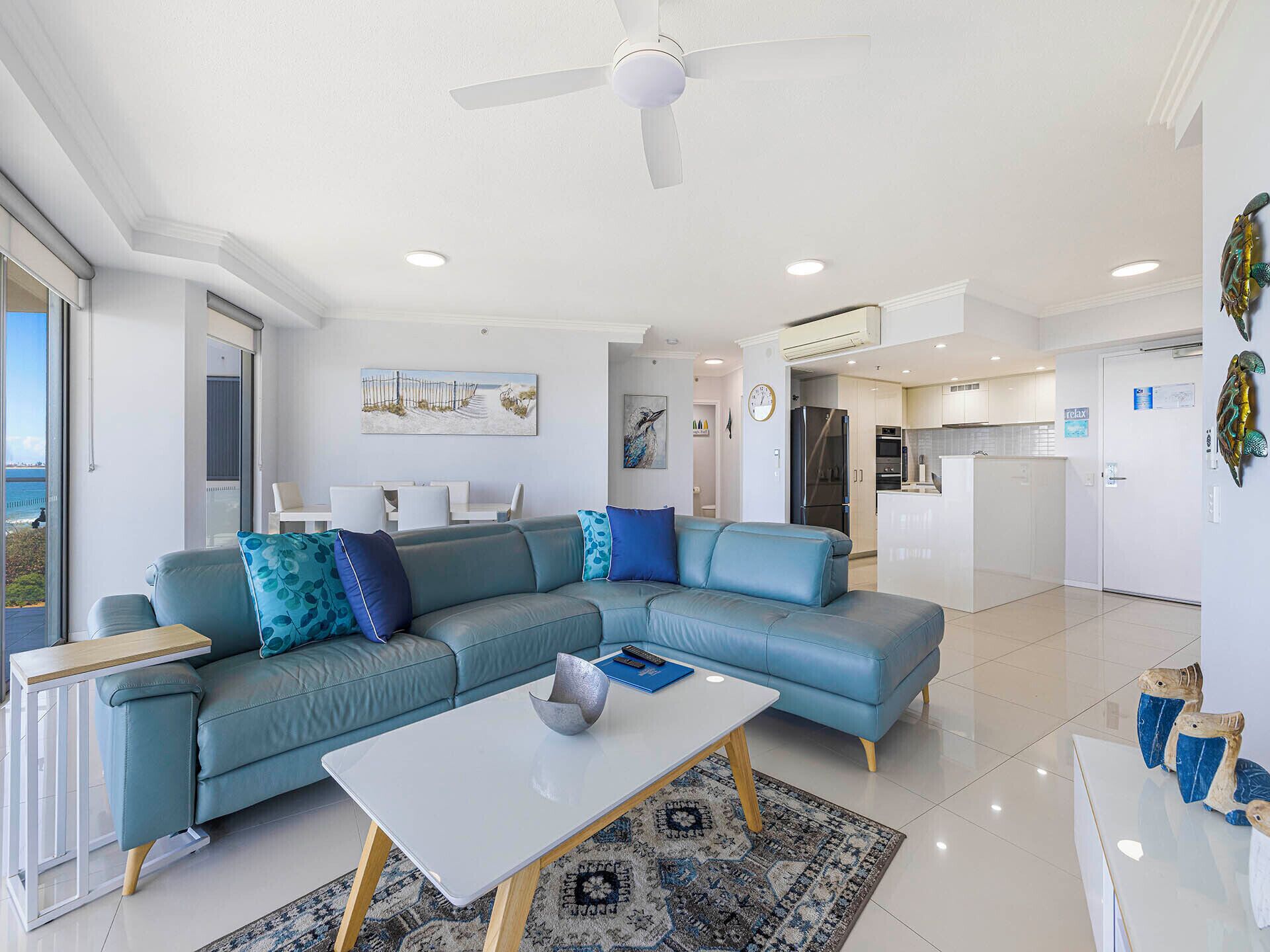 Un salon moderne avec un canapé d’angle, une table basse et un coin repas comprenant une table et des chaises blanches.