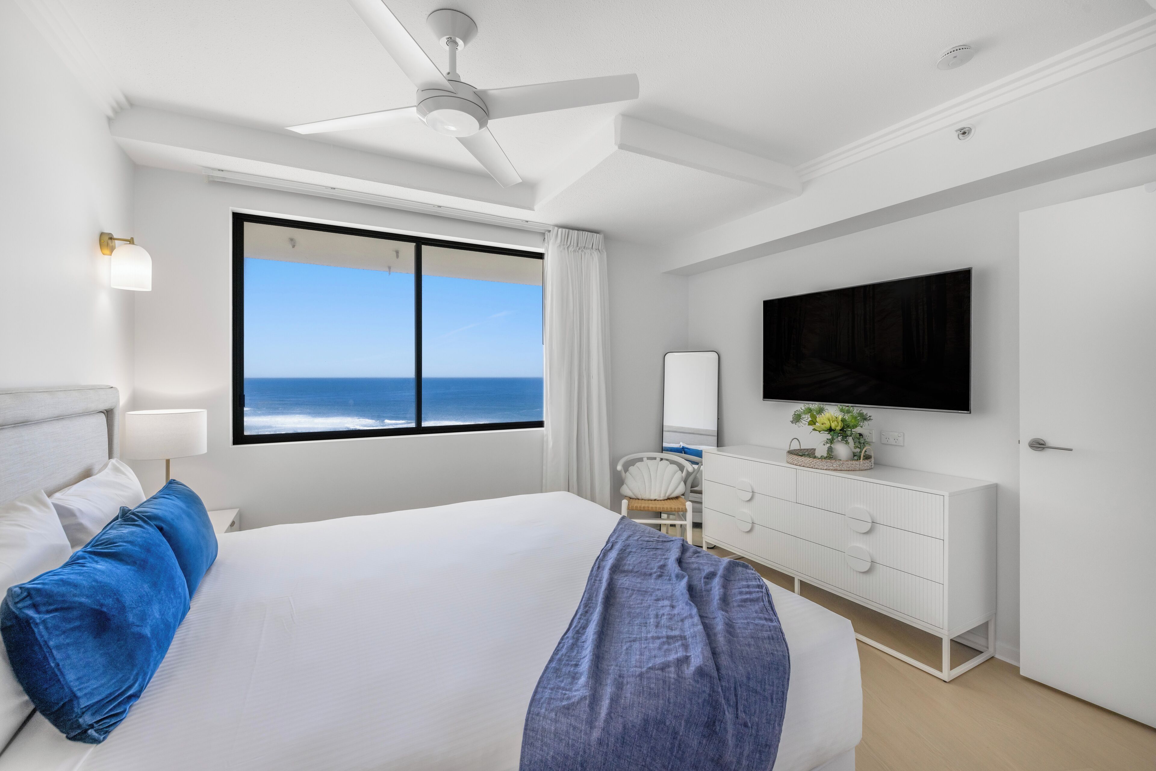 Une chambre d’hôtel avec un grand lit, un ventilateur de plafond, un téléviseur fixé au mur et une vue sur l’océan.
