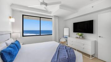 Une chambre d’hôtel avec un grand lit, un ventilateur de plafond, un téléviseur fixé au mur et une vue sur l’océan.