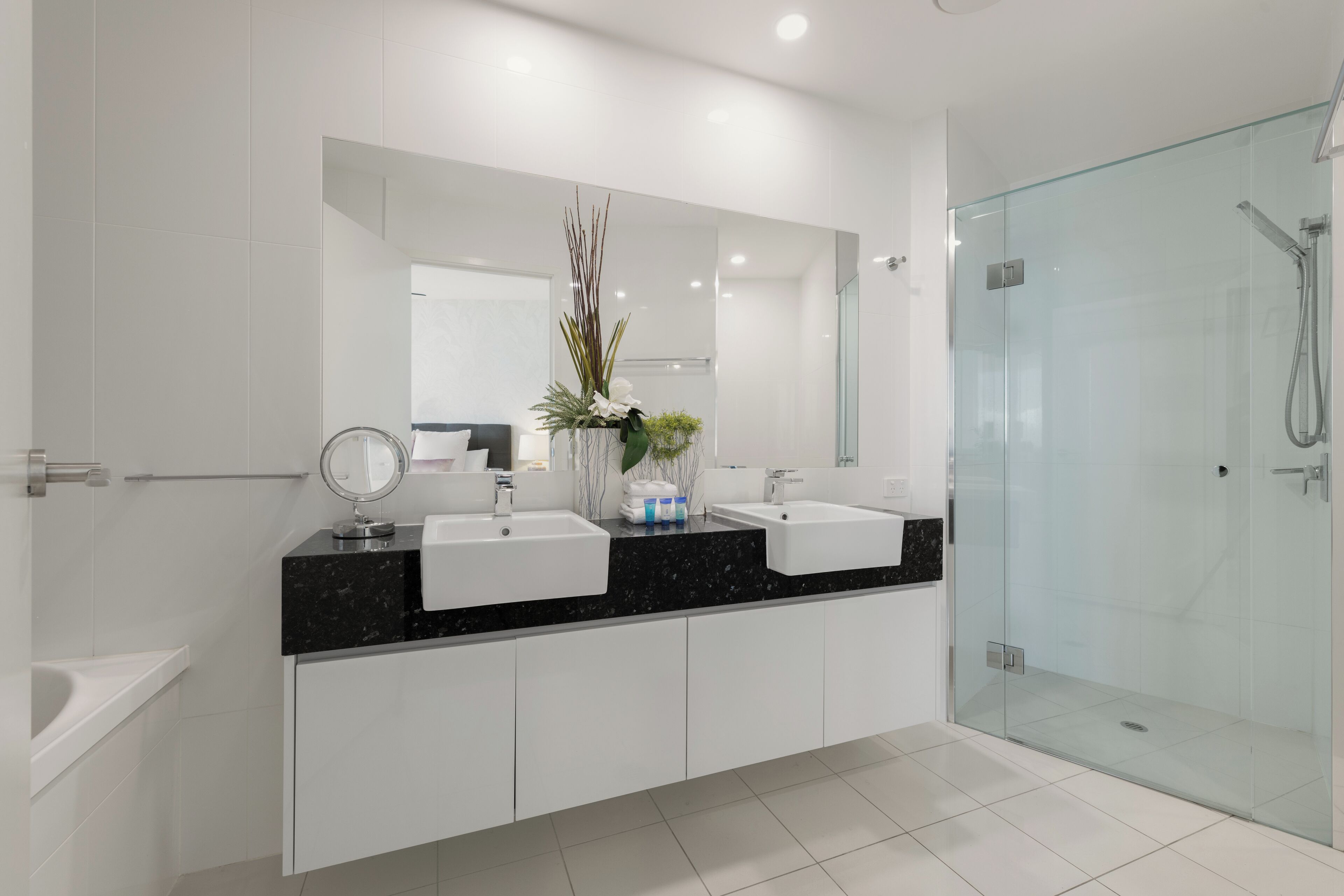 Een moderne badkamer met twee wastafels, een grote spiegel en een douche met glazen wanden.