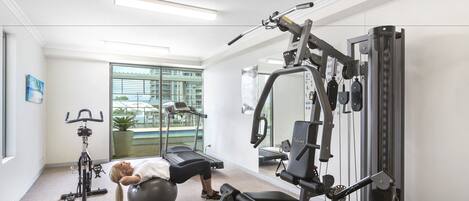 A gym with exercise equipment, a treadmill, and a large window with a view of a building and greenery.