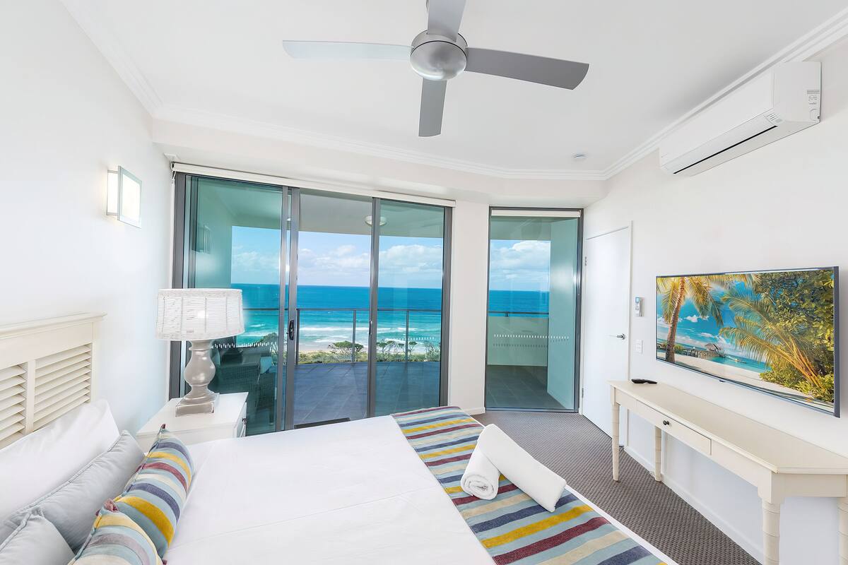 Ein modernes Hotelzimmer mit einem großen Bett, einem Deckenventilator, einem Fernseher und einem Balkon mit Blick aufs Meer.