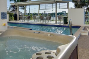 A hot tub with a pool view, outdoor seating, and a sign indicating emergency stop button use. - Beach on Sixth (Maroochydore)