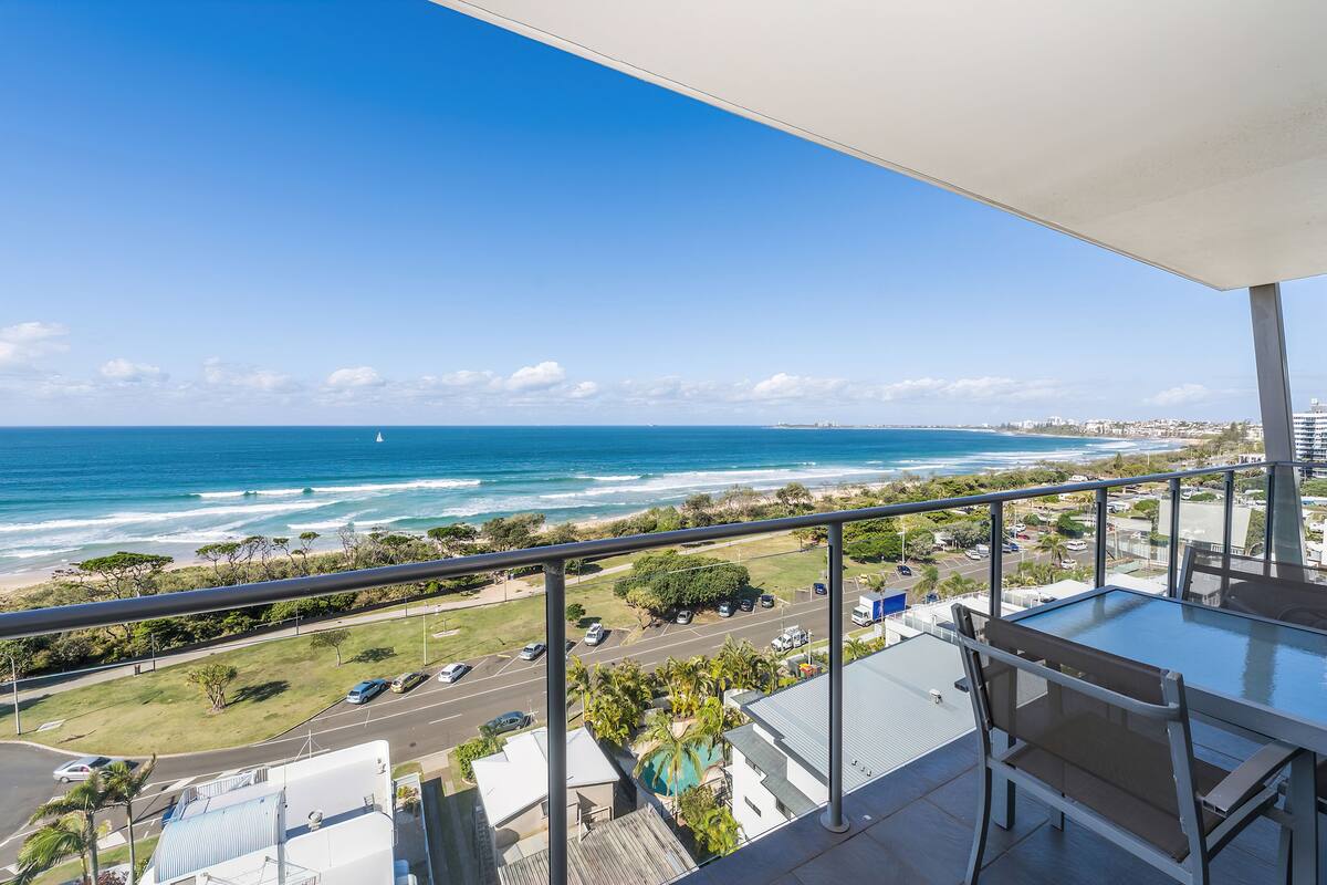 Ein Balkon mit Glastisch und Stühlen mit Blick auf Strand und Meer.