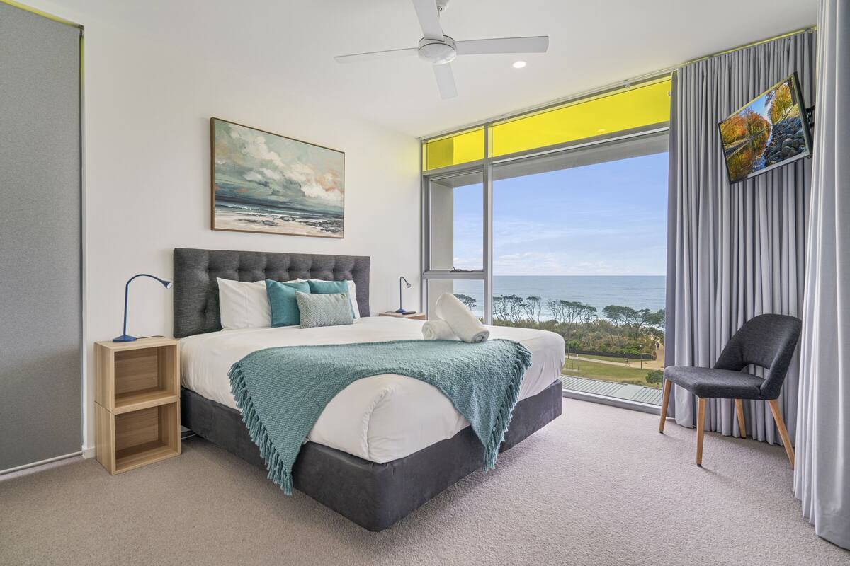 Ein Schlafzimmer mit einem großen Bett, Meerblick, Deckenventilator und einem an der Wand befestigten Fernseher.