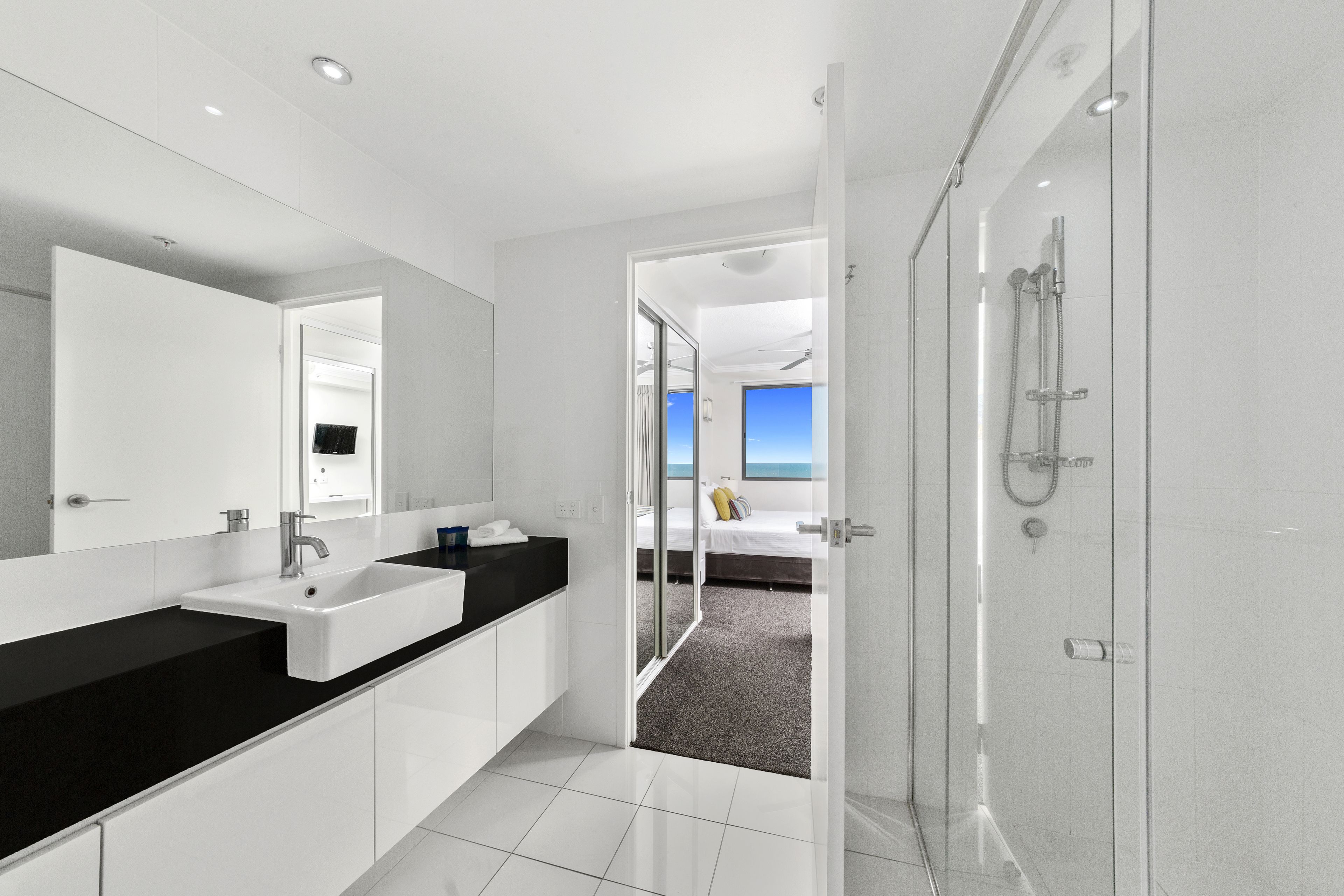 A modern bathroom with a large mirror, two sinks, and a shower area.