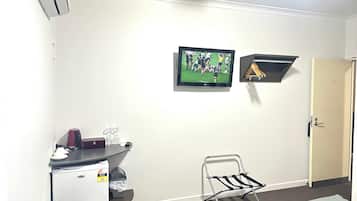 A hotel room with a bed, a desk with a computer, a chair, a TV mounted on the wall, and a door with a number.