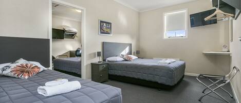 A hotel room with two beds, a desk, a chair, a TV, and a window.