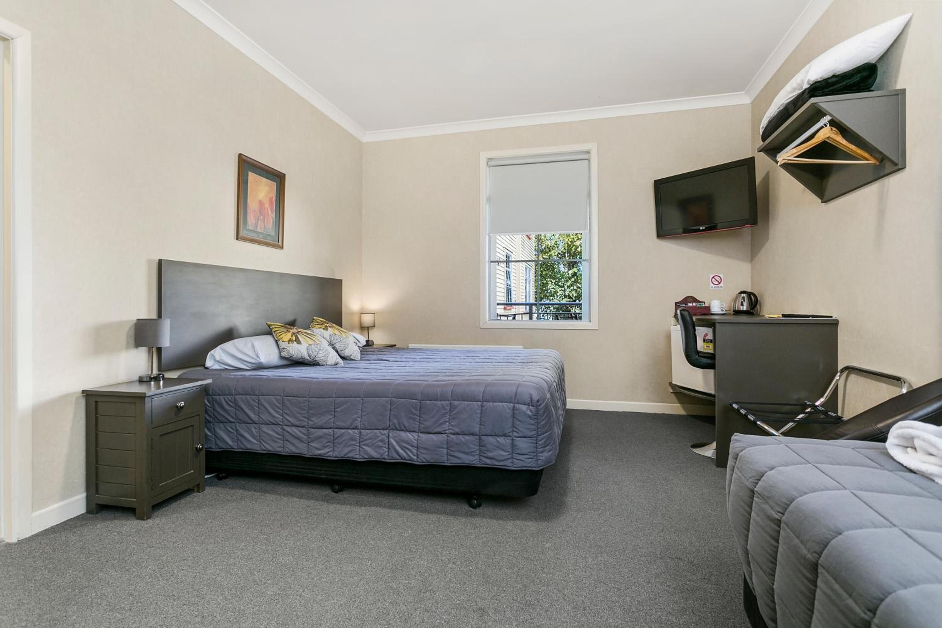 A bedroom with a bed, bedside table, lamp, TV, and a desk with a chair.