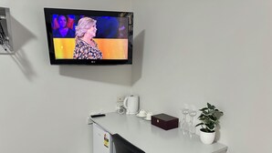 A hotel room with a white desk, a television mounted on the wall, a potted plant, a coffee maker, and a box. - No1 Motels On Victoria (Cambridge)