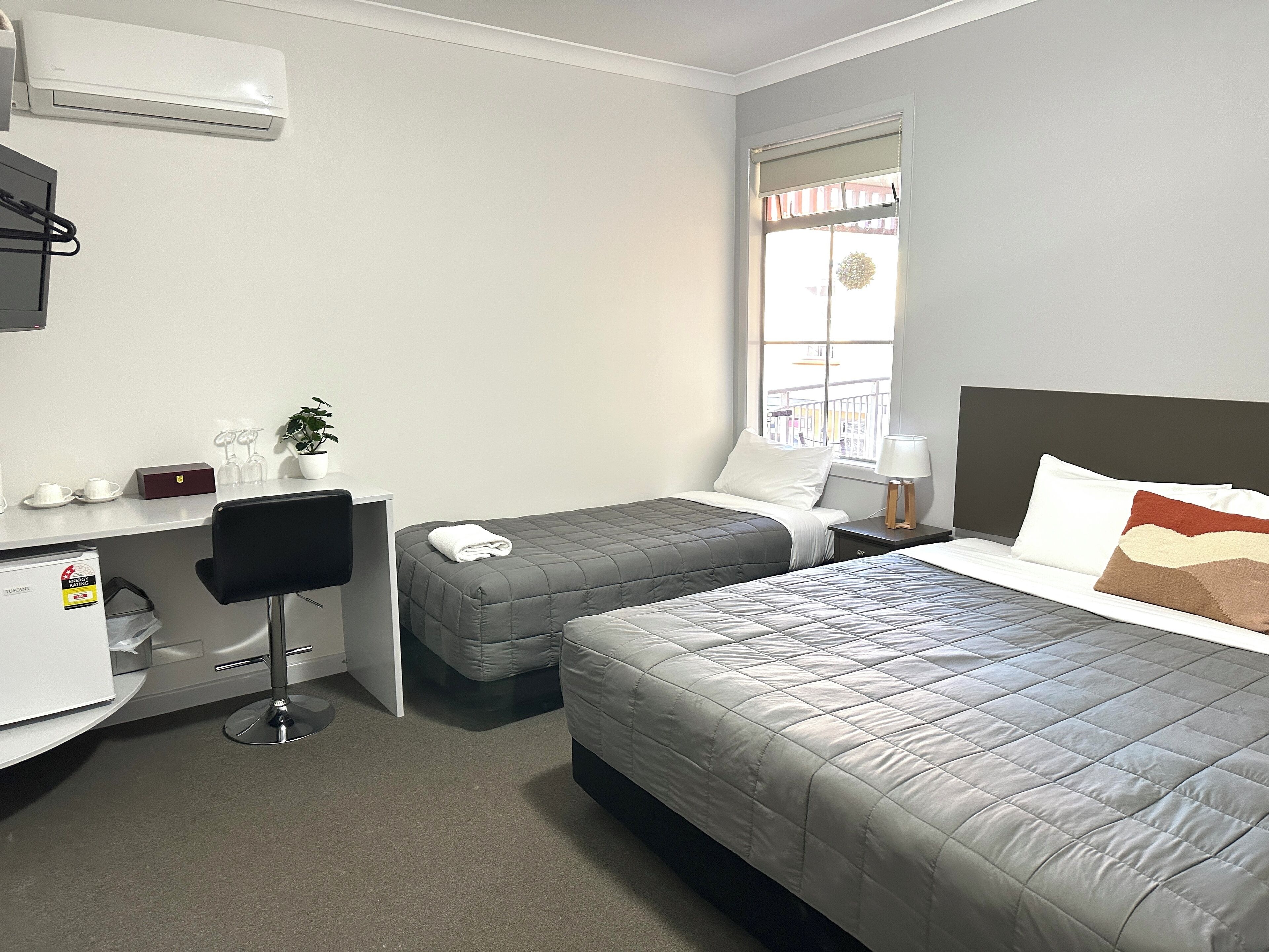 Habitación de hotel con cama, escritorio, silla, una mesita con una planta y ventana con vistas a un balcón.