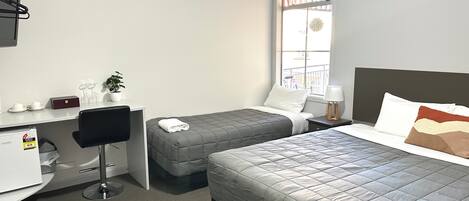 Habitación de hotel con cama, escritorio, silla, una mesita con una planta y ventana con vistas a un balcón.