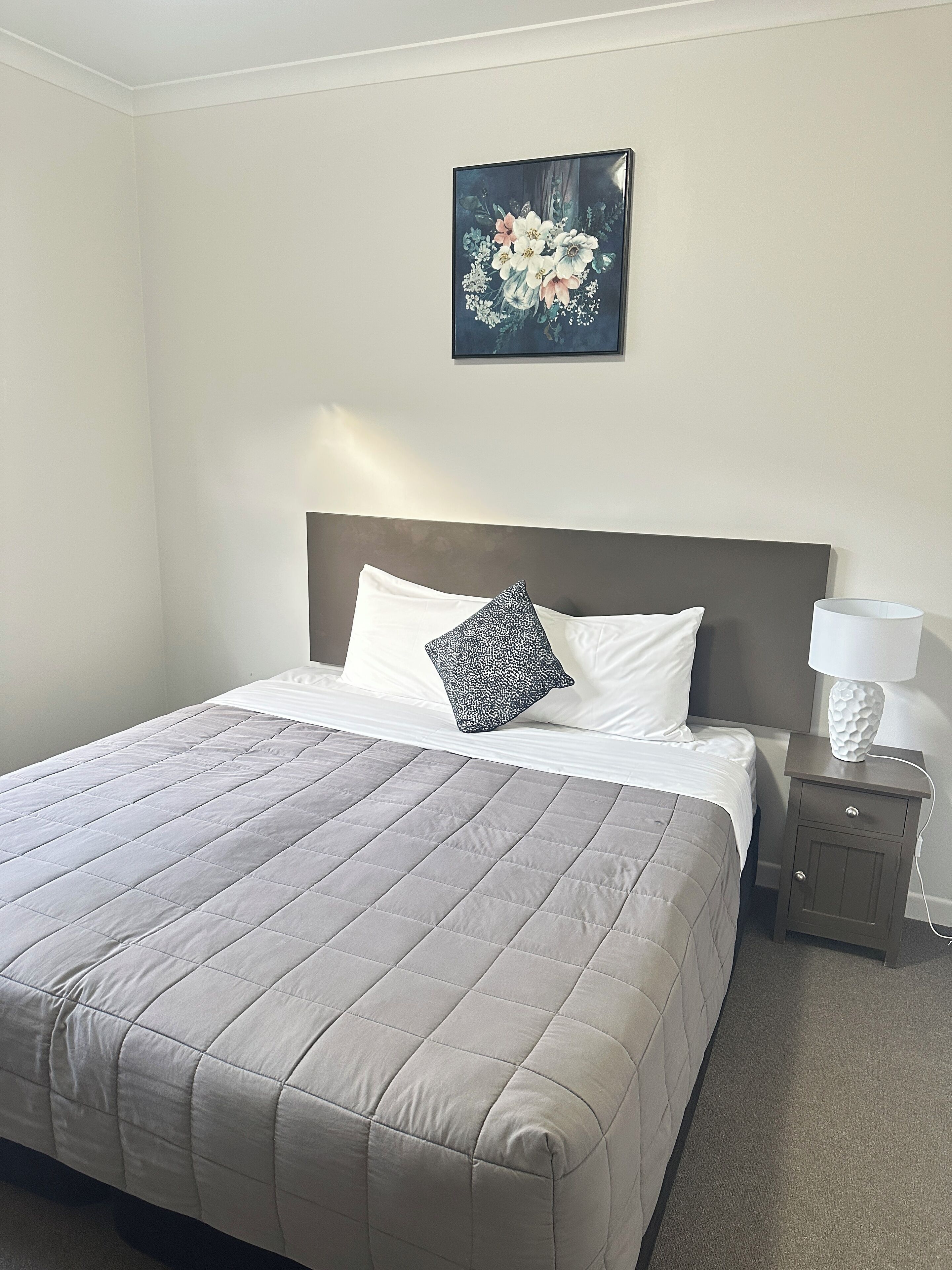 A neatly made bed with a quilted bedspread, a pillow, and a bedside table with a lamp.