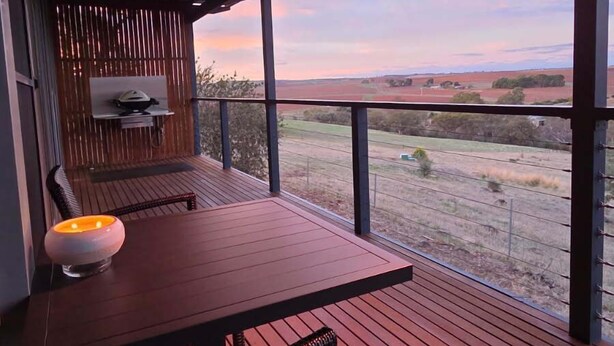 A covered outdoor area with a table and chairs, a small table with a candle, and a view of the landscape. - Barossa Pavilions (Lyndoch)
