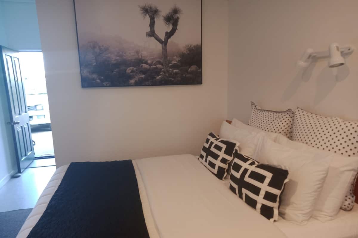A bedroom with a bed, pillows, a blanket, a wall-mounted light, and a door leading to a balcony.