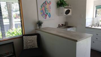 Een moderne keuken met een centraal eiland, een magnetron en een spoelbak. Op de muur hangt een kleurrijk kunstwerk en op het aanrecht staat een potplant.