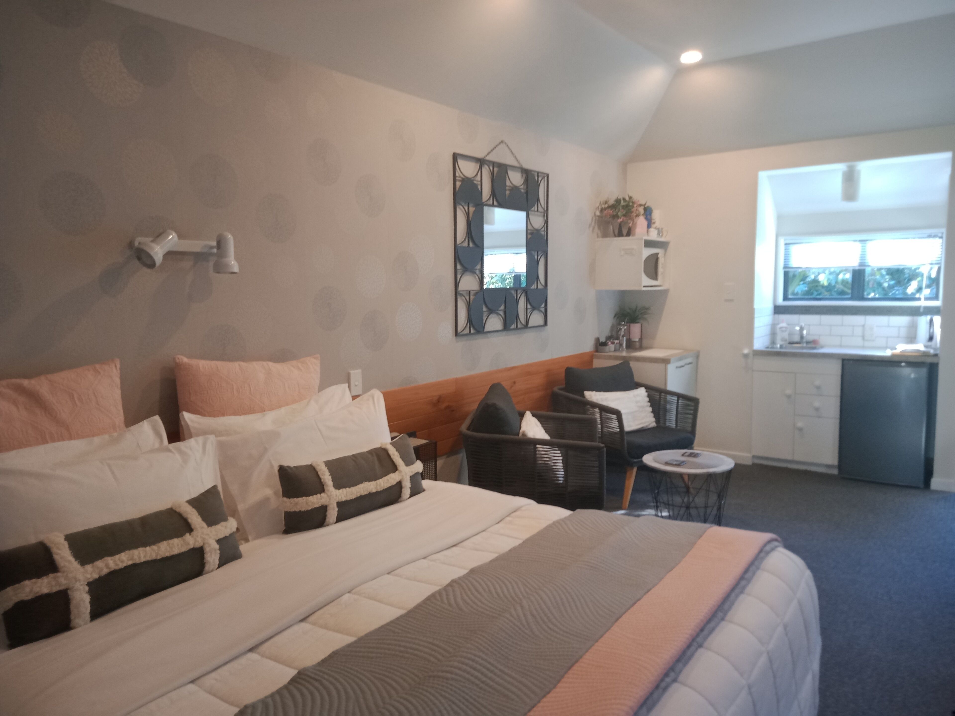 A hotel room with a bed, a small seating area, a kitchenette, and a window with a view.